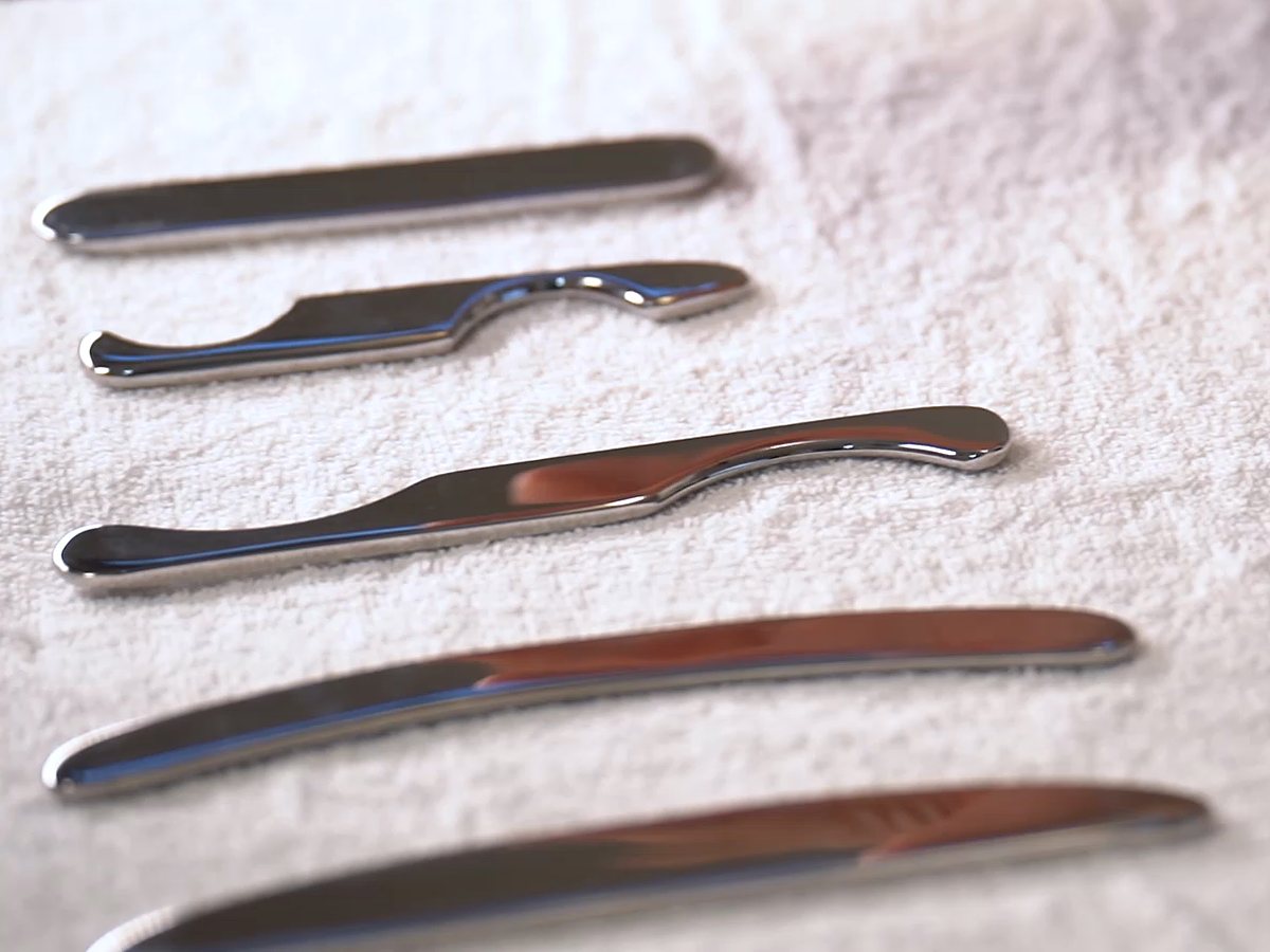 Five flat metal scraping tools of different shapes laid in a row on a white towel